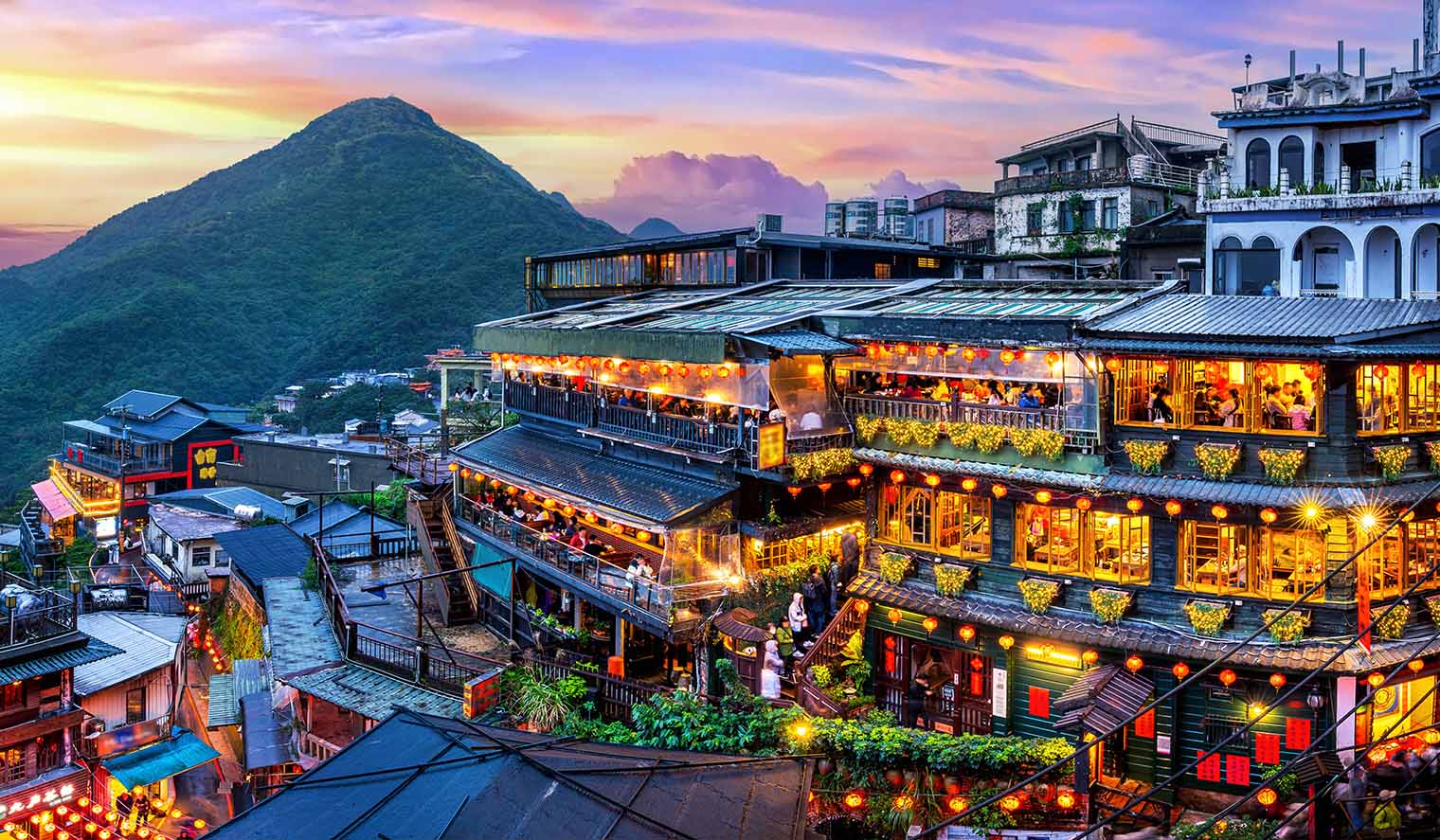 Abendliche Ansicht des malerischen Bergdorfes Jiufen auf Taiwan Reisen mit beleuchteten traditionellen Gebäuden, lebendigem Treiben und grünen Hügeln im Hintergrund.