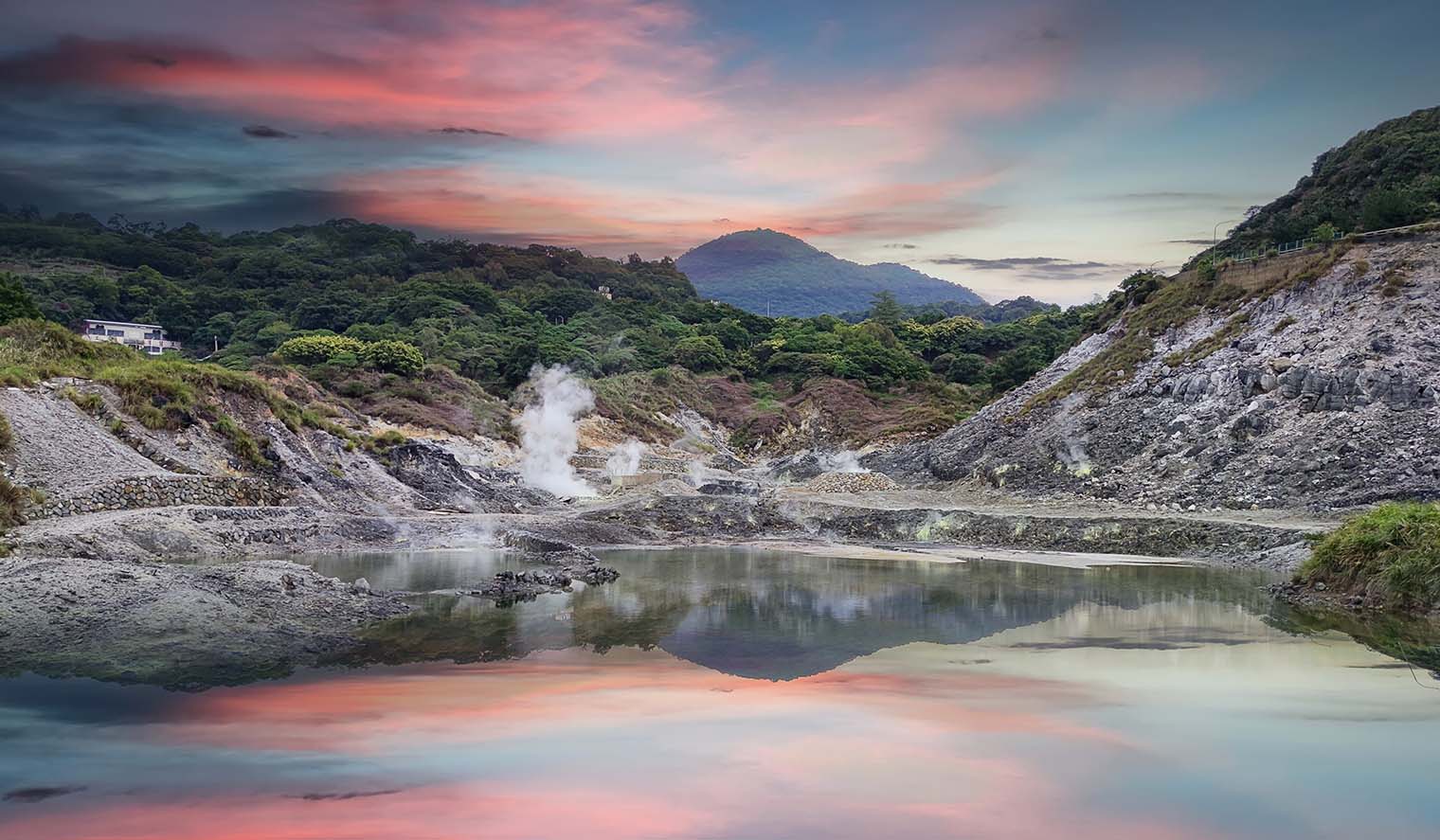 Landschaft im Yangmingshan Nationalpark auf Taiwan Reisen mit dampfenden Schwefelquellen, reflektierendem Wasser und bewaldeten Hügeln unter einem farbenfrohen Himmel bei Sonnenuntergang